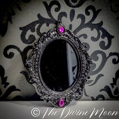 a mirror with pink stones on it sitting on top of a table next to a wall