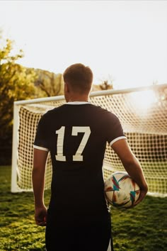 a man holding a soccer ball in front of a goalie net with the sun behind him