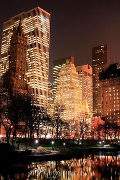 the city is lit up at night with lights reflecting in the water and trees on both sides