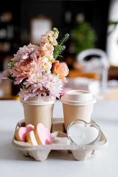 two coffee cups with flowers in them on a tray next to some cookies and marshmallows