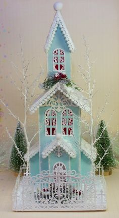 a blue and white church with snow on the roof, surrounded by small trees in front of it