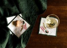 a glass of wine and two napkins on a wooden table with green linens