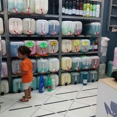 a little boy standing in front of a shelf filled with lots of water jugs