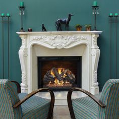 two chairs sitting in front of a fire place with candles on top of the fireplace