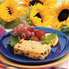 a blue plate topped with fruit next to sunflowers and grapes on a table