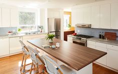 a kitchen with white cabinets and wooden counter tops, along with bar stools that match the hardwood flooring