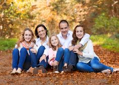 a family sitting on the ground in an autumn forest with leaves all around them and smiling at the camera