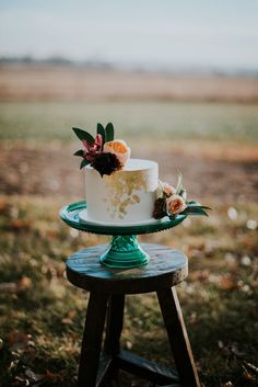 a white and gold cake sitting on top of a wooden table next to a field