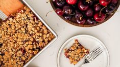 a piece of pie next to a bowl of cherries