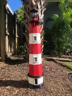 a red and white lighthouse sitting on top of a pile of mulch next to a fence