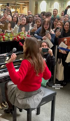 a woman sitting at a piano in front of a group of people holding microphones