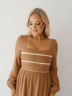 Twirl around in the "Wynn Dress!" This elevated maxi dress is perfect for church or work because of its modest design and fall color! It boasts a soft waffle print fabric, mocha base with ivory rick-rack along the bust, and long balloon sleeves. Easy to pair with boots or heels to complete the look! Detailed Fit: Square neckline maxi dress Cinching at top of shoulder Tie at back of neckline Zipper in the back Waffle pattern throughout skirt Double-lined Overfall Fit: Fitted through bust with a r Fall V-neck Dress With Smocked Back, Brown Maxi Dress With Smocked Back, Beige Long Sleeve Smocked Dress, Brown Smocked Bodice Dress, Midi Length, Beige V-neck Rayon Dress, Long Balloons, Rick Rack, Fall Color, Square Necklines