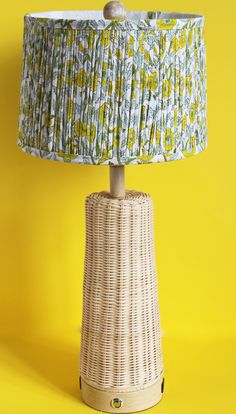 a wicker table lamp with a blue and yellow fabric shade on the top, against a bright yellow background