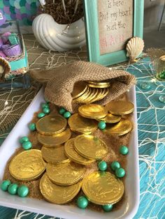 a table topped with lots of gold coins and green bead necklaces next to a blue frame