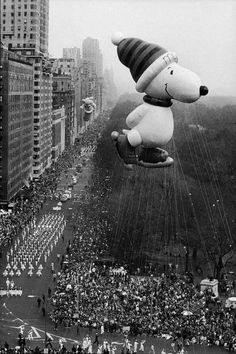 a large balloon with a dog on it flying in the air over a city filled with people