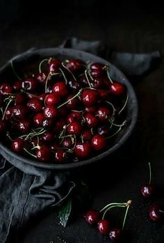 a bowl filled with cherries on top of a wooden table next to a cloth