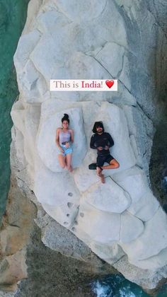 two people are sitting on some rocks by the water and there is a sign that says, this is india