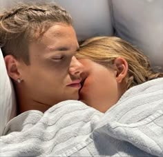 a man and woman laying in bed with their eyes close to each other as they kiss