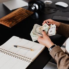 a woman is counting money on her desk with a pen and notepad in front of her