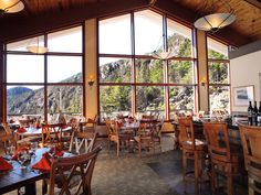 a restaurant with large windows and wooden tables in front of the mountain view is shown