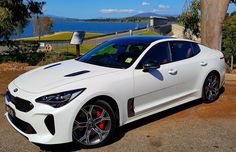 a white sports car parked in front of a lake