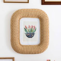 a wicker frame with flowers in it on a wooden table next to a white wall