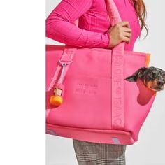 a woman carrying a pink tote bag with a small dog in the front pocket