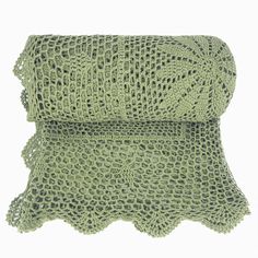 a green crocheted blanket on top of a white surface with an openwork design