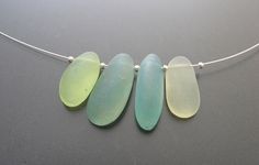 three pieces of sea glass are hanging from a silver necklace on a white cord,