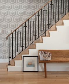 a wooden bench sitting under a stair case next to a wall with geometric designs on it