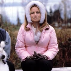 two people sitting on a bench with a dog in their lap and one person wearing a hat