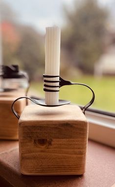 a wooden block with a white candle on it sitting next to a window sill