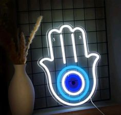 a blue and white hamsa hand with an evil eye on it is lit up in the dark