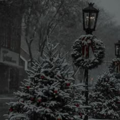 two christmas trees with wreaths on them in front of a lamp post and street light