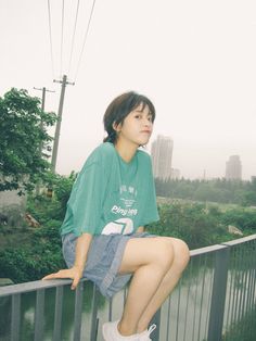 a young woman sitting on top of a metal rail next to a river and power lines