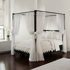 a canopy bed with white sheets and curtains on it's sides, in front of a window