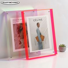 two clear acrylic frames with pictures on them and a plant in the background