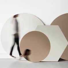 a blurry photo of a person walking past large circular objects on the floor in front of a white wall