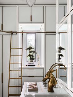 a room with white walls and gold accents, including a ladder leading to the window