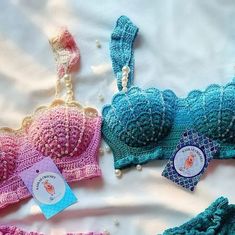 three crocheted bras are laying on a white sheet and one is blue, the other has pink