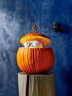 a pumpkin with googly eyes sitting on top of a piece of wood in front of a blue wall