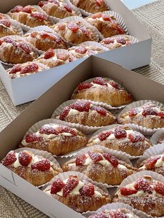 two boxes filled with pastries covered in powdered sugar and strawberries on top of a table