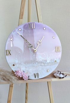 a pink clock with roman numerals on the face sitting on a wooden shelf