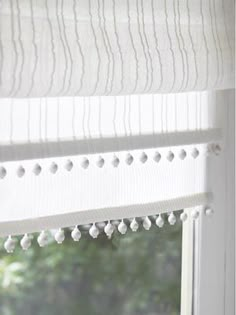 a window with white curtains and pom - poms hanging from the valance