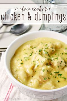 a white bowl filled with chicken and dumplings on top of a table next to silverware