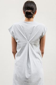 a woman standing with her back turned to the camera and wearing a grey shirt dress