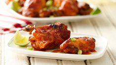 two plates filled with chicken wings covered in sauce and garnished with green onions