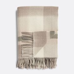 a beige and white plaid blanket with fringes on the bottom, in front of a gray