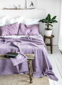 a bed with purple sheets and pillows in a white room next to a wooden table