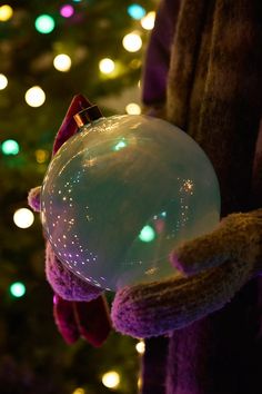 a person holding an inflatable snowball next to a christmas tree with lights